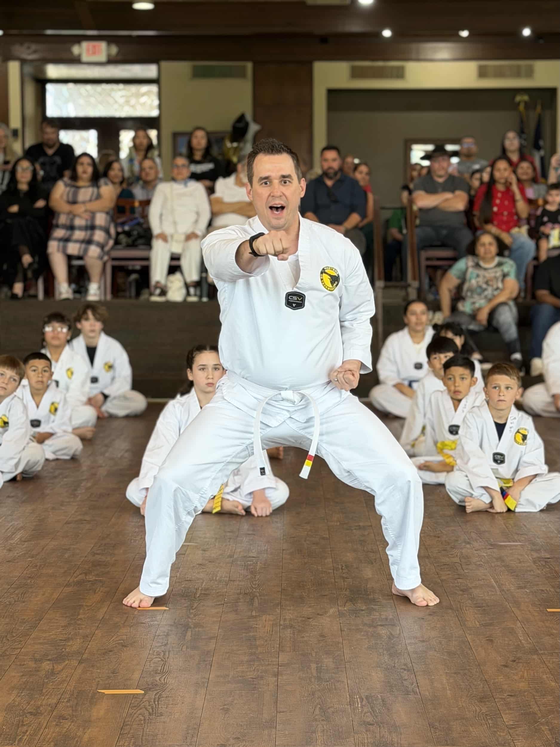 US Taekwondo Conroe instructor punching from squat stance in front of class of students in gi.